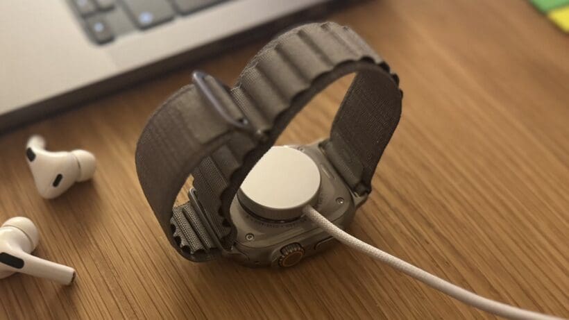 apple watch ultra on charge next to airpods and macbook